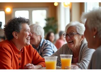 A lively group of seniors laughing and socializing over healthy refreshments in a bright community event space.